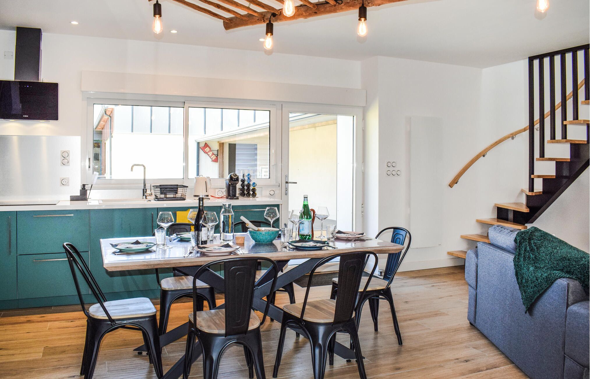 A modern kitchen with a dining area, wooden flooring, and a staircase.