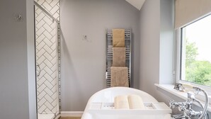 A modern bathroom with a freestanding bathtub, a towel rack with multiple towels, and a window providing a view of greenery outside. - 6 Hillside Cottages (Gainsborough)