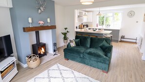 A living room with a fireplace, a sofa, a TV, and a kitchen in the background. - 6 Hillside Cottages (Gainsborough)