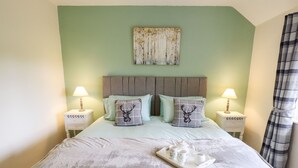 A neatly made bed with a tray of white cups and a floral mug, flanked by two bedside tables with lamps, in a room with a green wall and a painting above the bed. - 6 Hillside Cottages (Gainsborough)