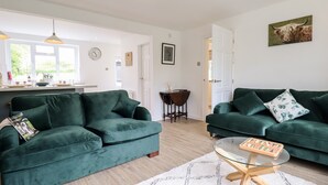 A modern living room with two green sofas, a glass coffee table, and a white rug. - 6 Hillside Cottages (Gainsborough)