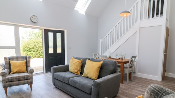 A modern living room with a grey sofa, plaid armchair, and yellow cushions. A dining table with chairs is visible in the background. - Willow Cottage (Ilfracombe)