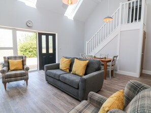 A modern living room with a grey sofa, plaid armchair, and yellow cushions. A dining table with chairs is visible in the background. - Willow Cottage (Ilfracombe)