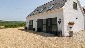 A modern white cottage with a sloped roof, large sliding glass doors, and a gravel driveway. - Willow Cottage (Ilfracombe)