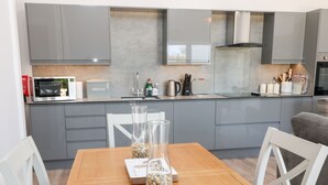 A modern kitchen with grey cabinets, a microwave, and a dining table with chairs. - Willow Cottage (Ilfracombe)