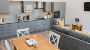 A modern kitchen with grey cabinets, a dining table with chairs, and a grey sofa. - Willow Cottage (Ilfracombe)