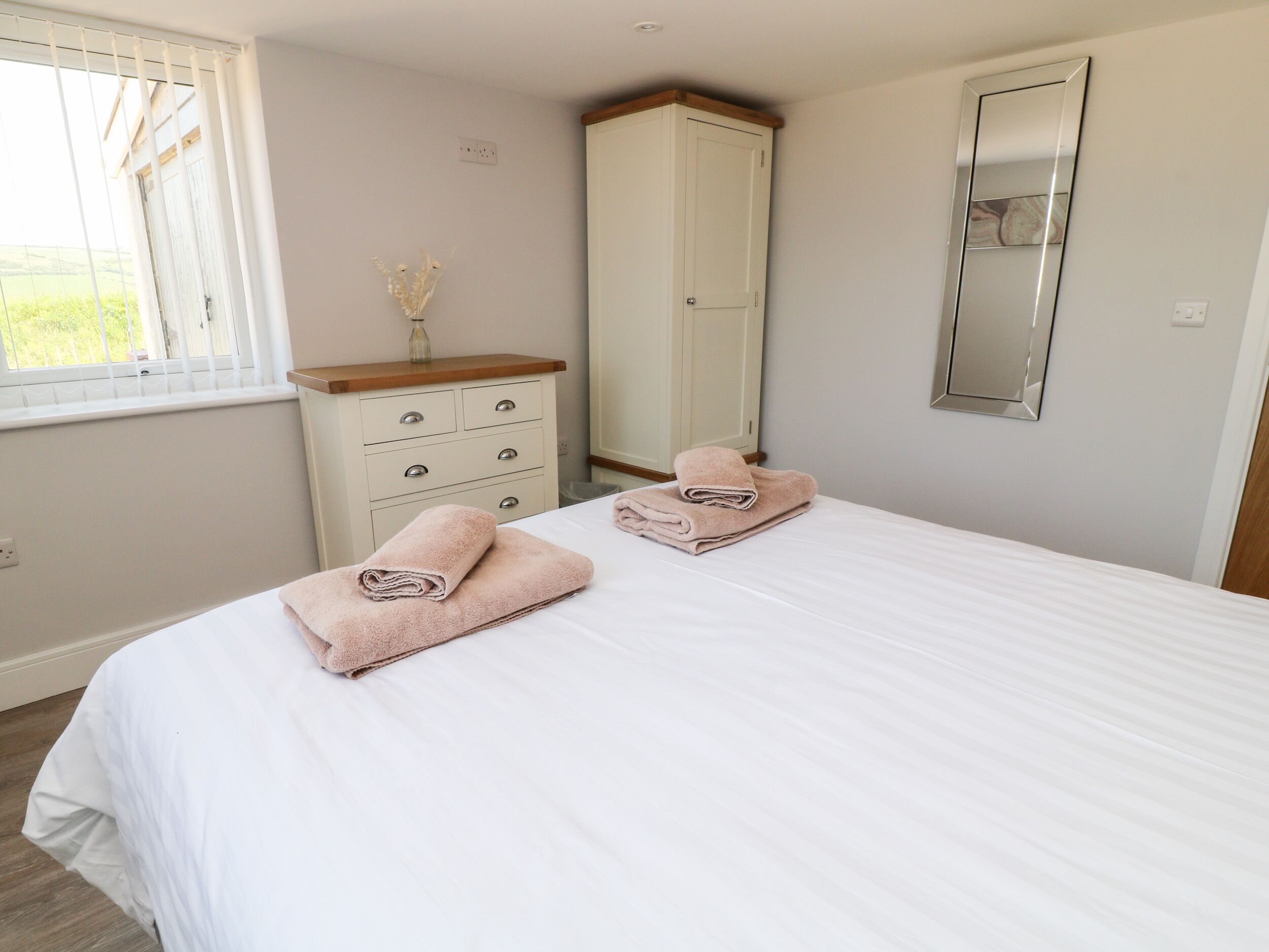A bedroom with a bed, a dresser, a mirror, and a window with blinds.
