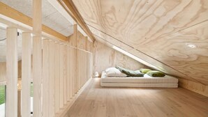 Ein modernes Schlafzimmer im Loft-Stil mit schrägem Dach, Holzbalken und einem eingebauten Bett mit Kissen.