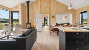 Ein modernes Interieur mit einer großen Holzbalkendecke, einem zentralen Kamin, einem Essbereich und einer Küche mit einer großen Kochinsel.