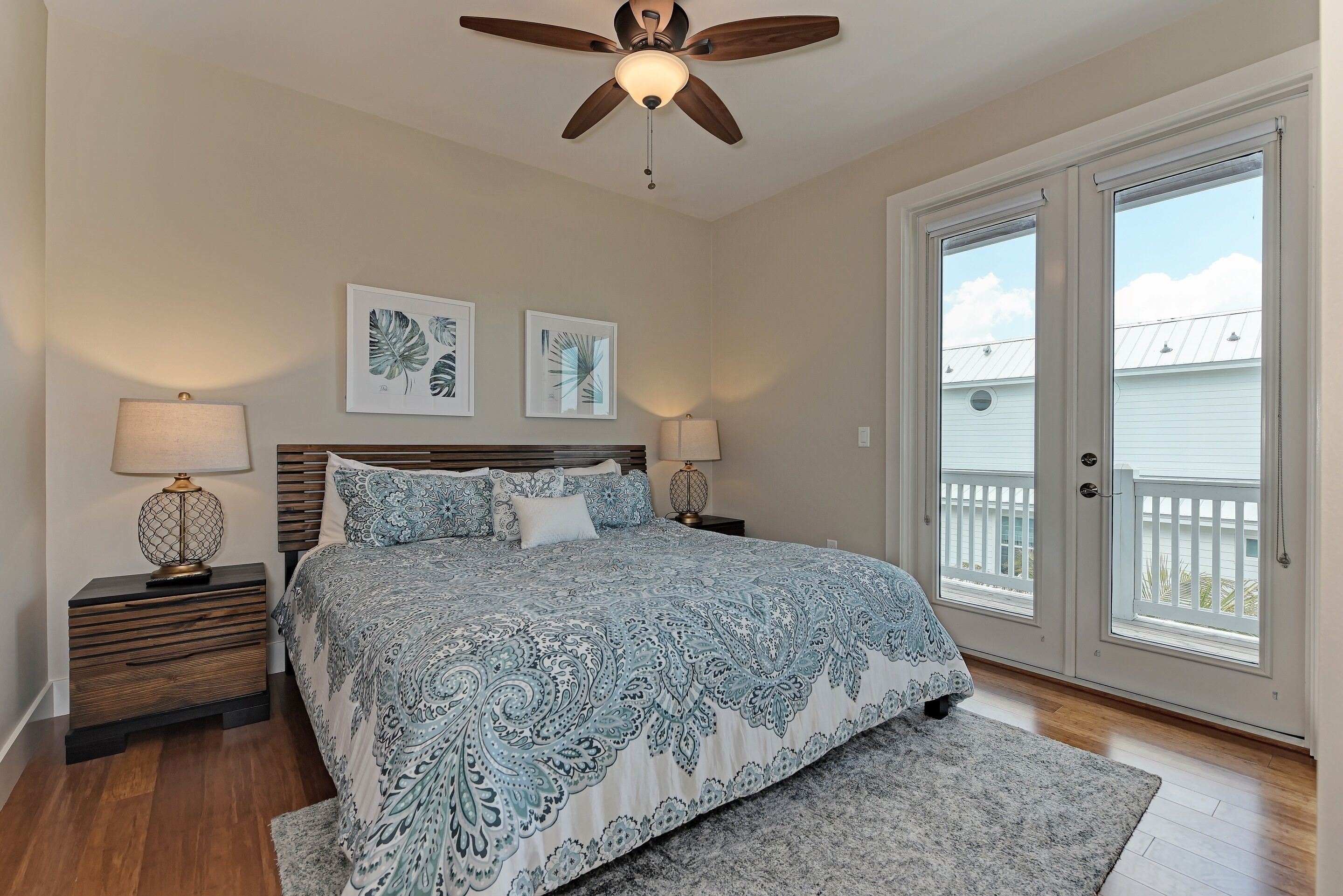 A bedroom with a bed, two nightstands, a ceiling fan, and a large sliding glass door leading to a balcony.