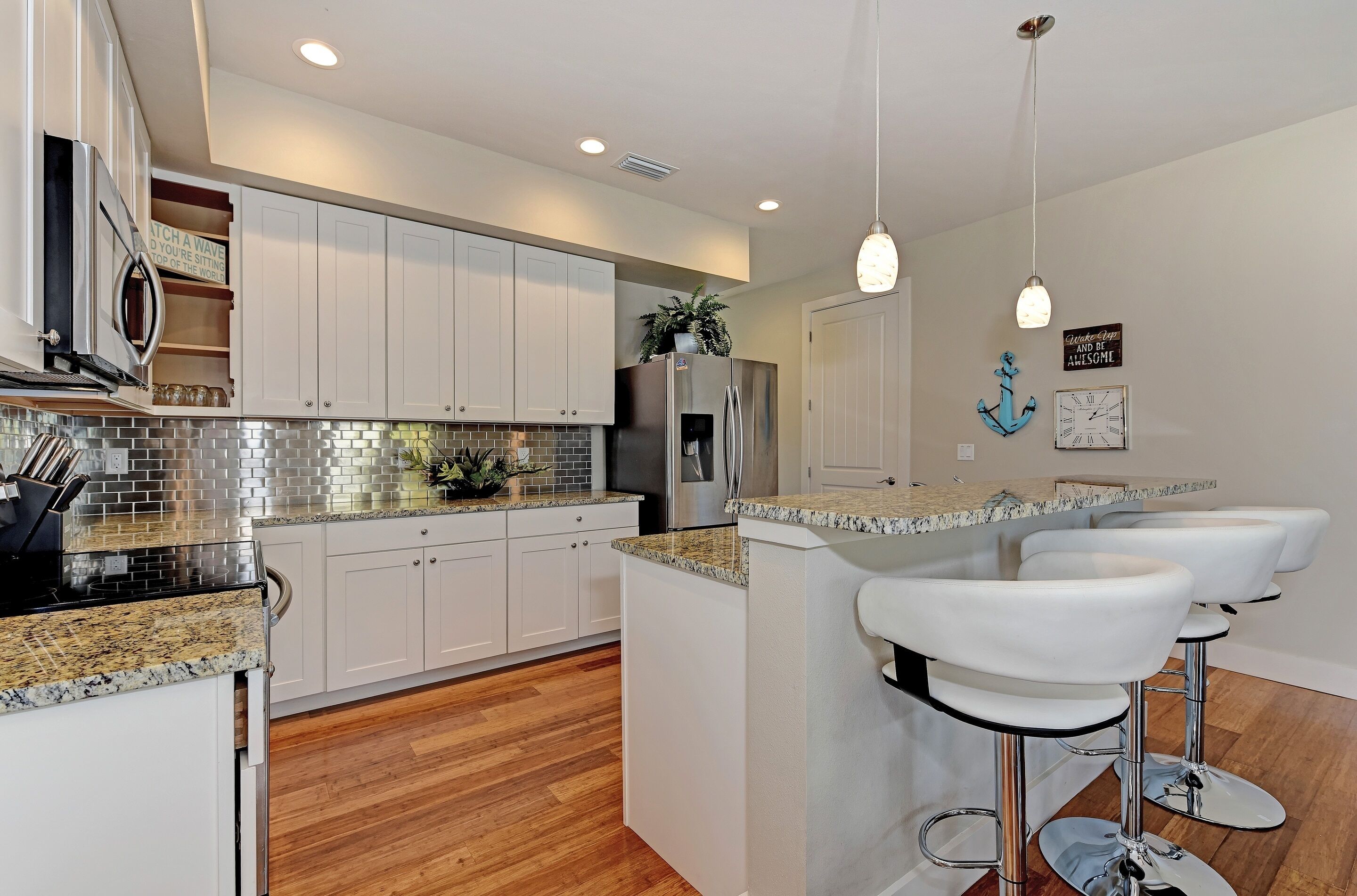 A modern kitchen with white cabinets, a granite countertop, and a built-in island with bar stools.