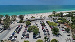 Eine Vogelperspektive auf einen Parkplatz am Strand mit Autos, einer Straße und einem Strand mit Menschen und Sonnenschirmen.