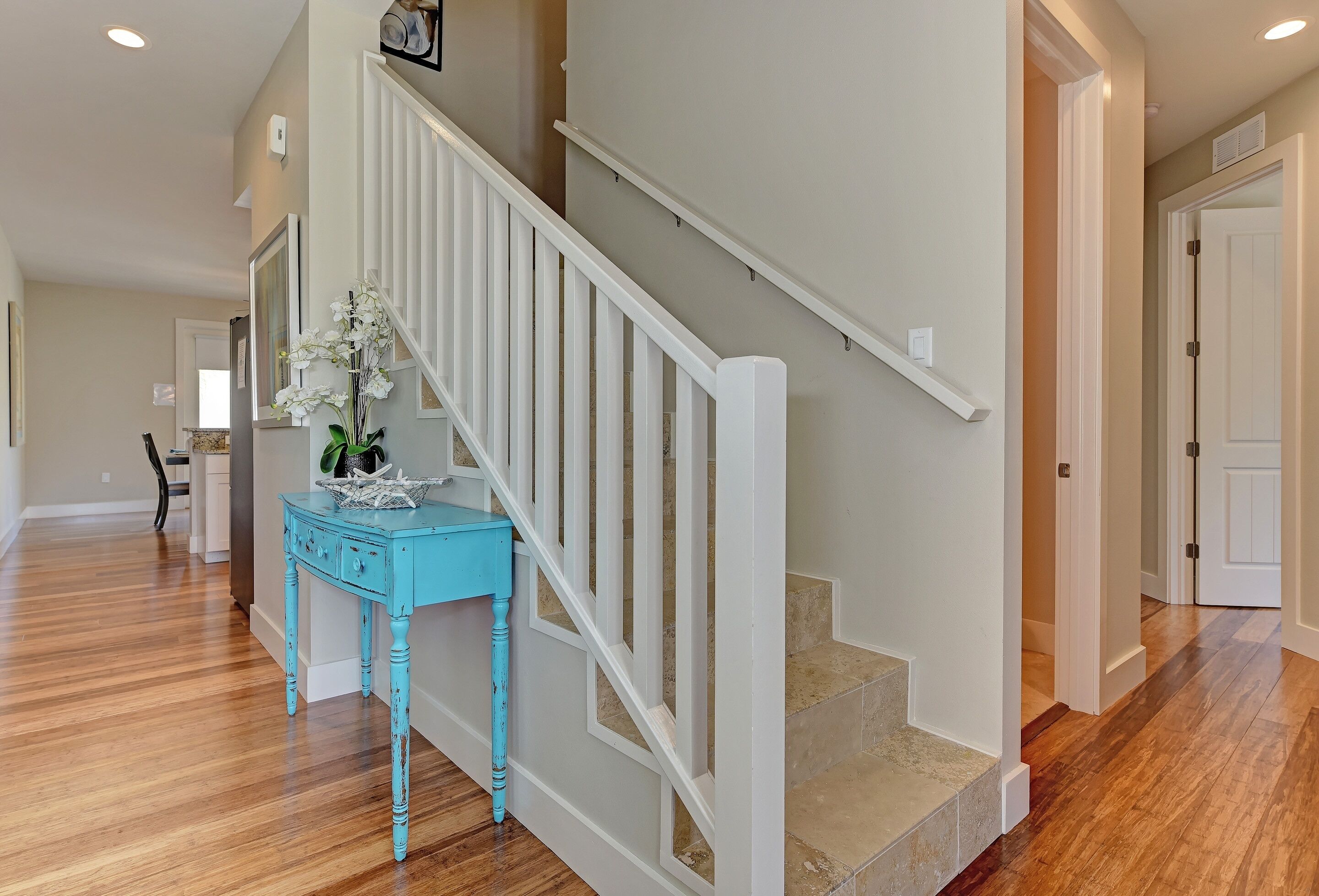 Una escalera con barandillas blancas, una mesita lateral turquesa con una planta, y suelo de madera.