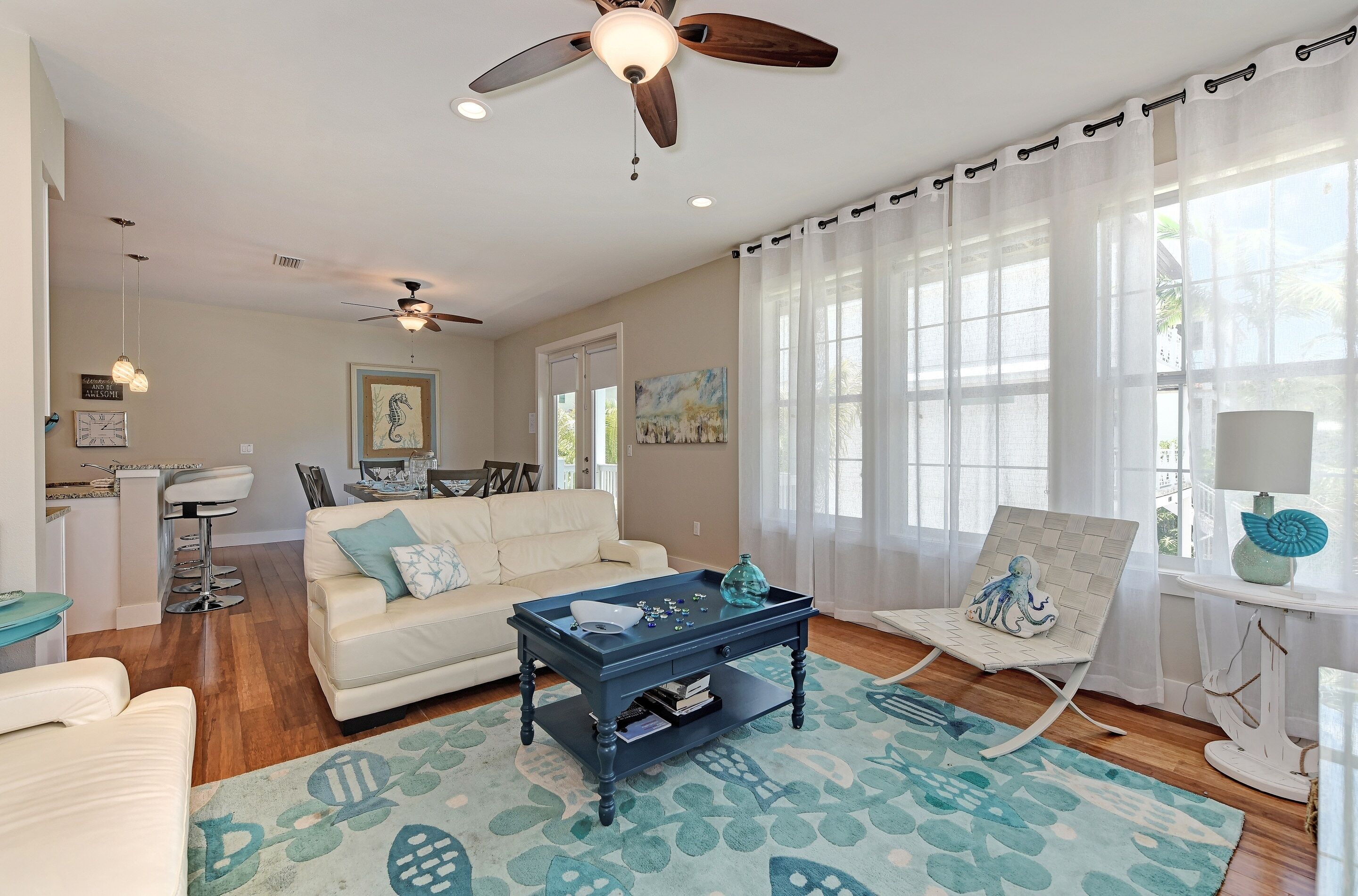 A spacious living room with a white sofa, a blue coffee table, and a ceiling fan.