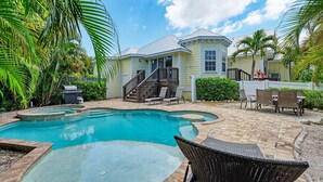 A backyard with a swimming pool, a covered patio, and a two-story house. - Starfish Isle managed by Beach Retreats (Holmes Beach)