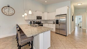 A modern kitchen with white cabinetry, a granite countertop, stainless steel appliances, and pendant lighting. - Starfish Isle managed by Beach Retreats (Holmes Beach)