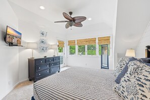 A bedroom with a bed, a ceiling fan, a dresser, a TV, and a window with a view of trees. - 4e Windermere By The Sea 4 Bedroom Villa (Myrtle Beach)