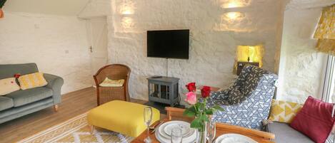 A cozy living room with a wooden dining table set for four, a comfortable sofa, a wicker chair, and a small fireplace.