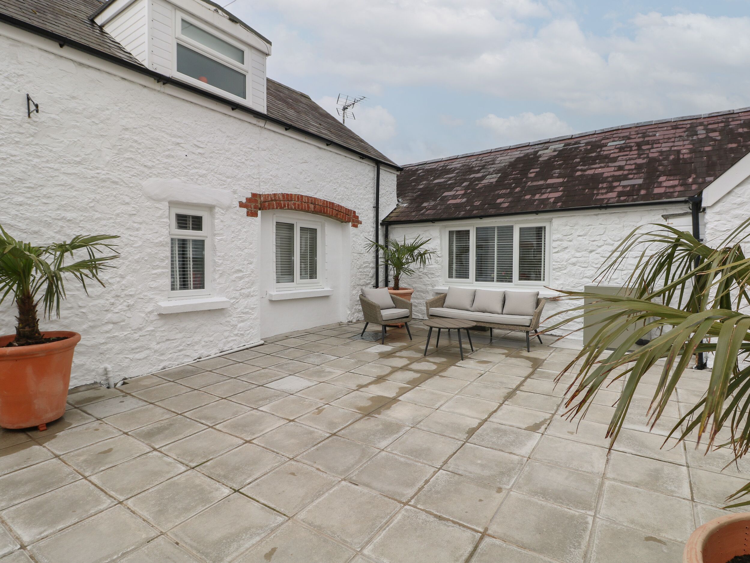 A white building with a tiled patio, two windows, and a brick feature.