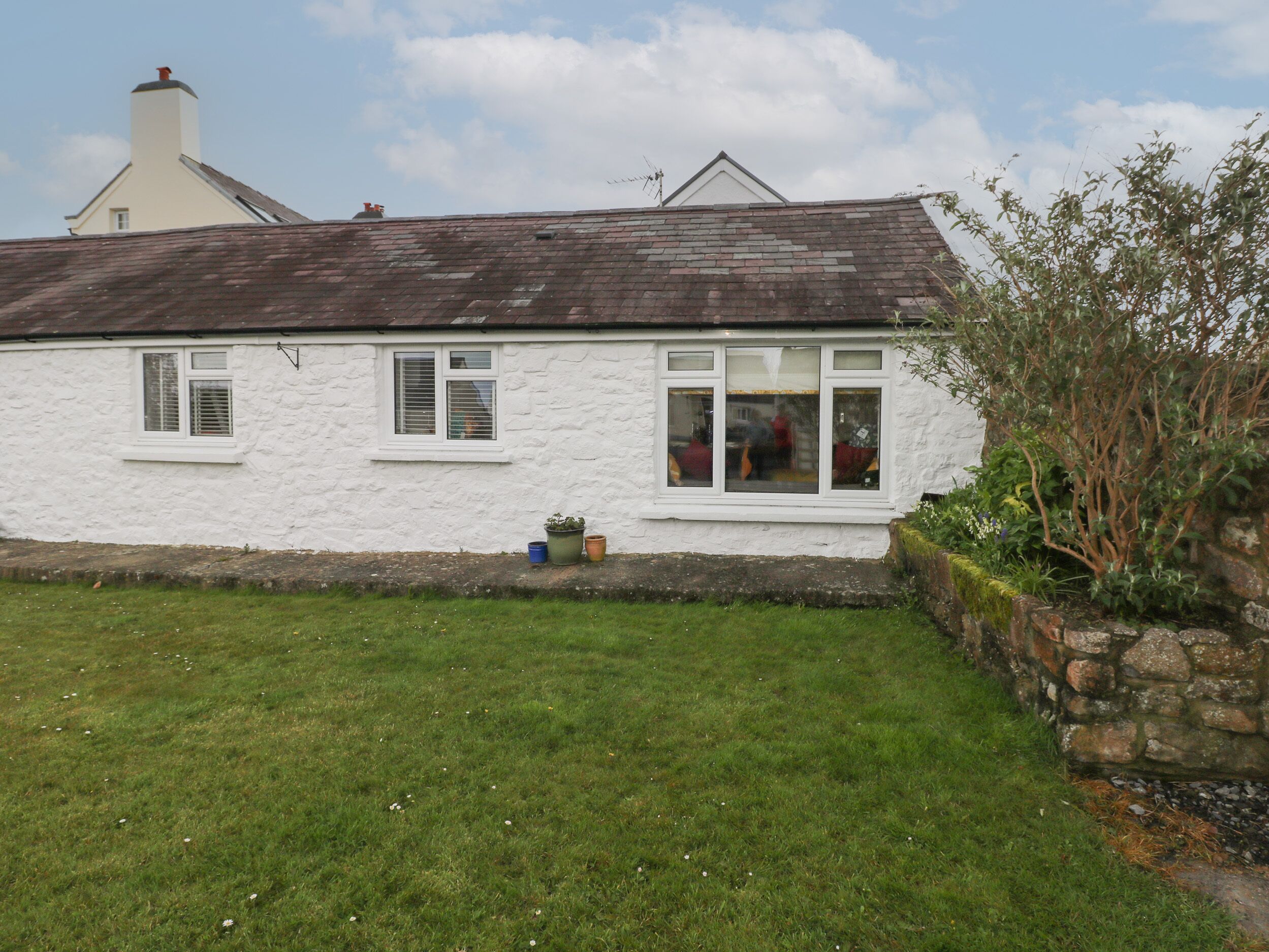A white cottage with a sloped roof, a stone wall, and a grassy yard.