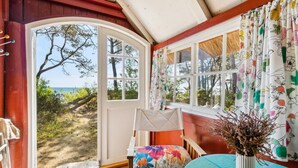 A cozy room with a large window offering a view of the beach and trees. - Cozy home in Nexø with kitchen (Nexø)