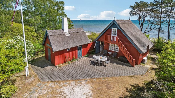 A red wooden house with a thatched roof, a wooden deck, and a view of the sea. - Cozy home in Nexø with kitchen (Nexø)