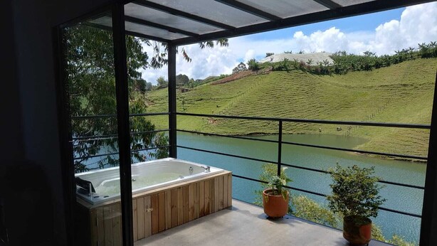 Un balcon doté d’un jacuzzi et agrémenté de plantes en pot, offrant une vue sur une étendue d’eau et un paysage verdoyant.