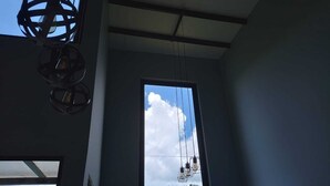 Une pièce dotée d’une grande fenêtre, d’un luminaire au plafond et offrant une vue sur un paysage verdoyant.