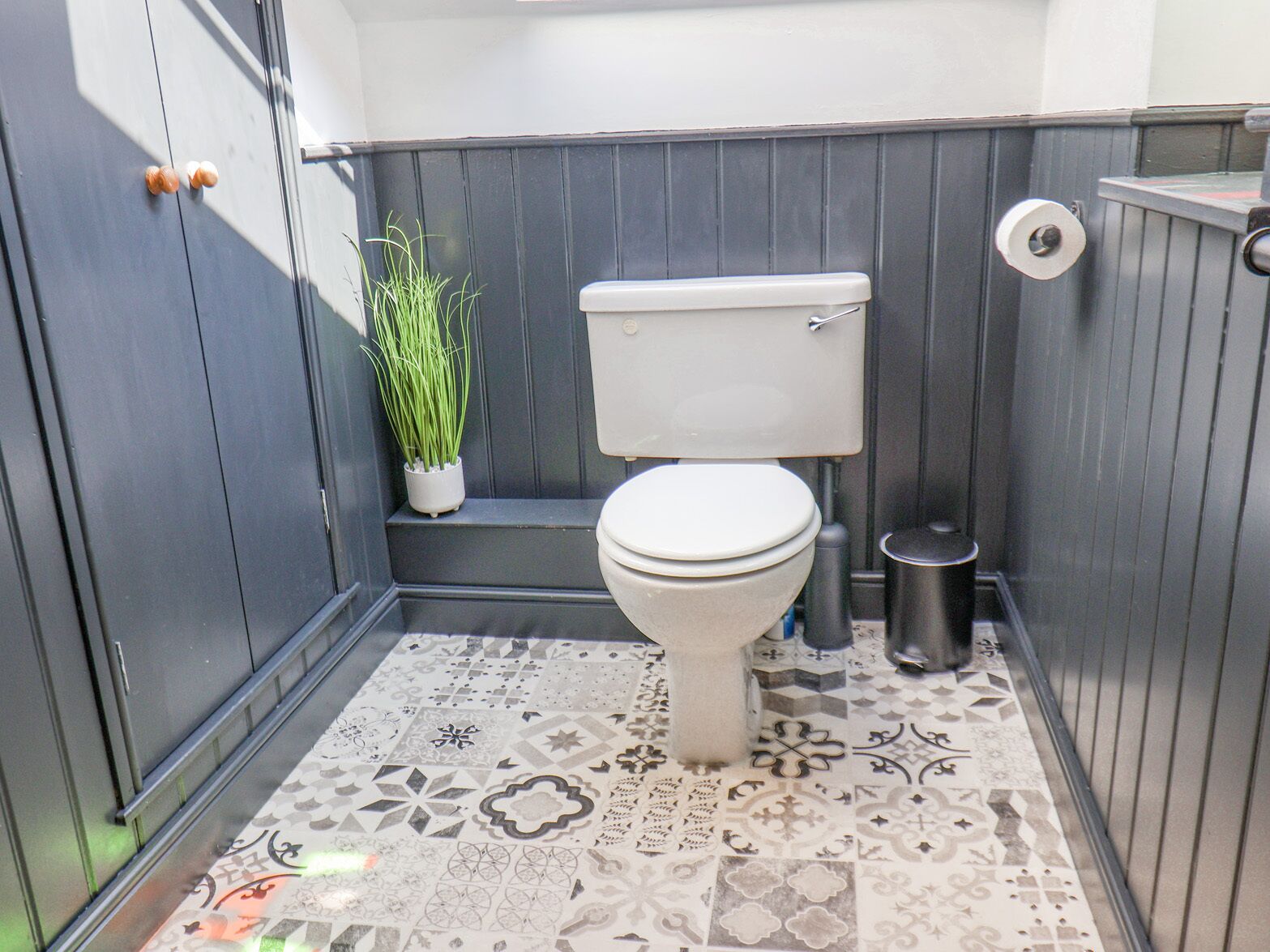 A compact bathroom with a toilet, a small trash bin, and a potted plant.