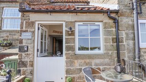 Un rustico in pietra con una porta bianca, una finestra e un piccolo patio con tavolo e sedia.