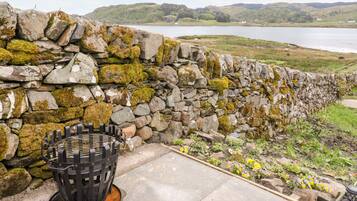 A stone wall with a metal grill, a concrete pathway, and a flower bed with yellow and purple flowers.
