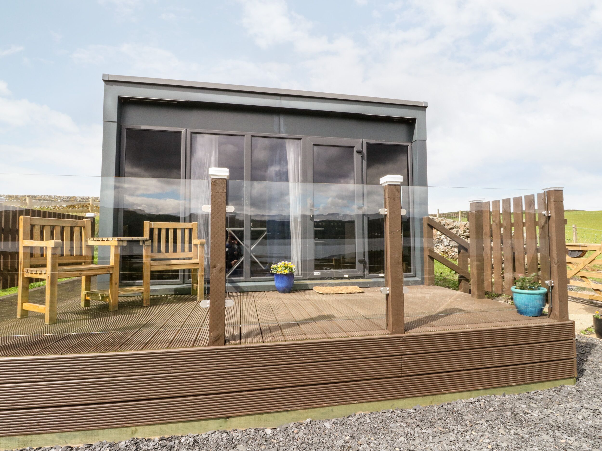 A modern building with large windows, a wooden deck, and outdoor seating.