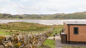 Ein rustikales Blockhaus mit Steinwand und Blick auf einen See und Hügel.