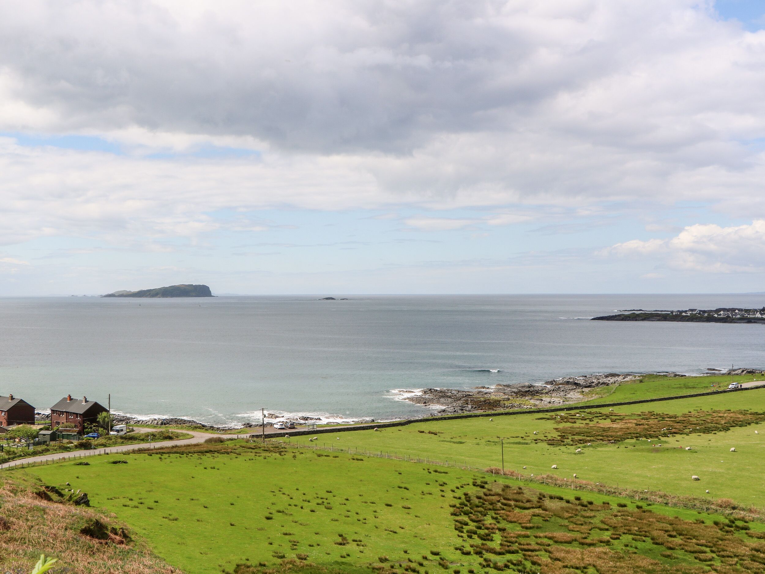 A coastal landscape with a grassy field, a rocky shoreline, and a distant island.