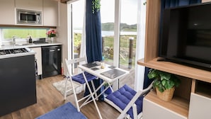 Eine moderne Küche mit Mikrowelle, Herd und Spüle, ein Essbereich mit Tisch und Stühlen sowie ein großes Fenster mit Blick auf einen See und Hügel.