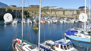 A marina with multiple boats docked, a rocky shoreline, and a building in the background. - The Hawthorns Large Detached 3 Bedroom Family Home (Seaham)