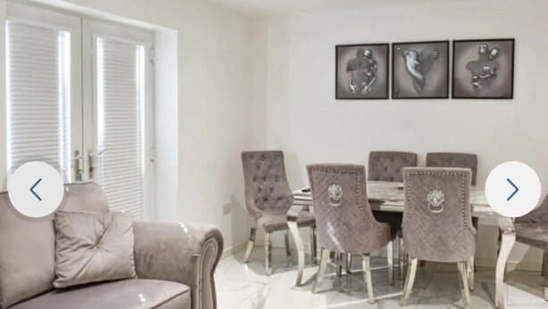 A dining area with a table and chairs, a sofa, and three framed artworks on the wall. - The Hawthorns Large Detached 3 Bedroom Family Home (Seaham)