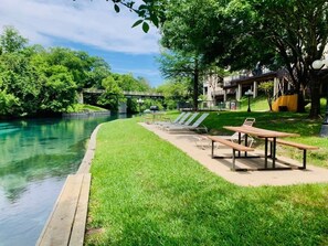 Un parque junto al río con mesas de picnic y sillones.