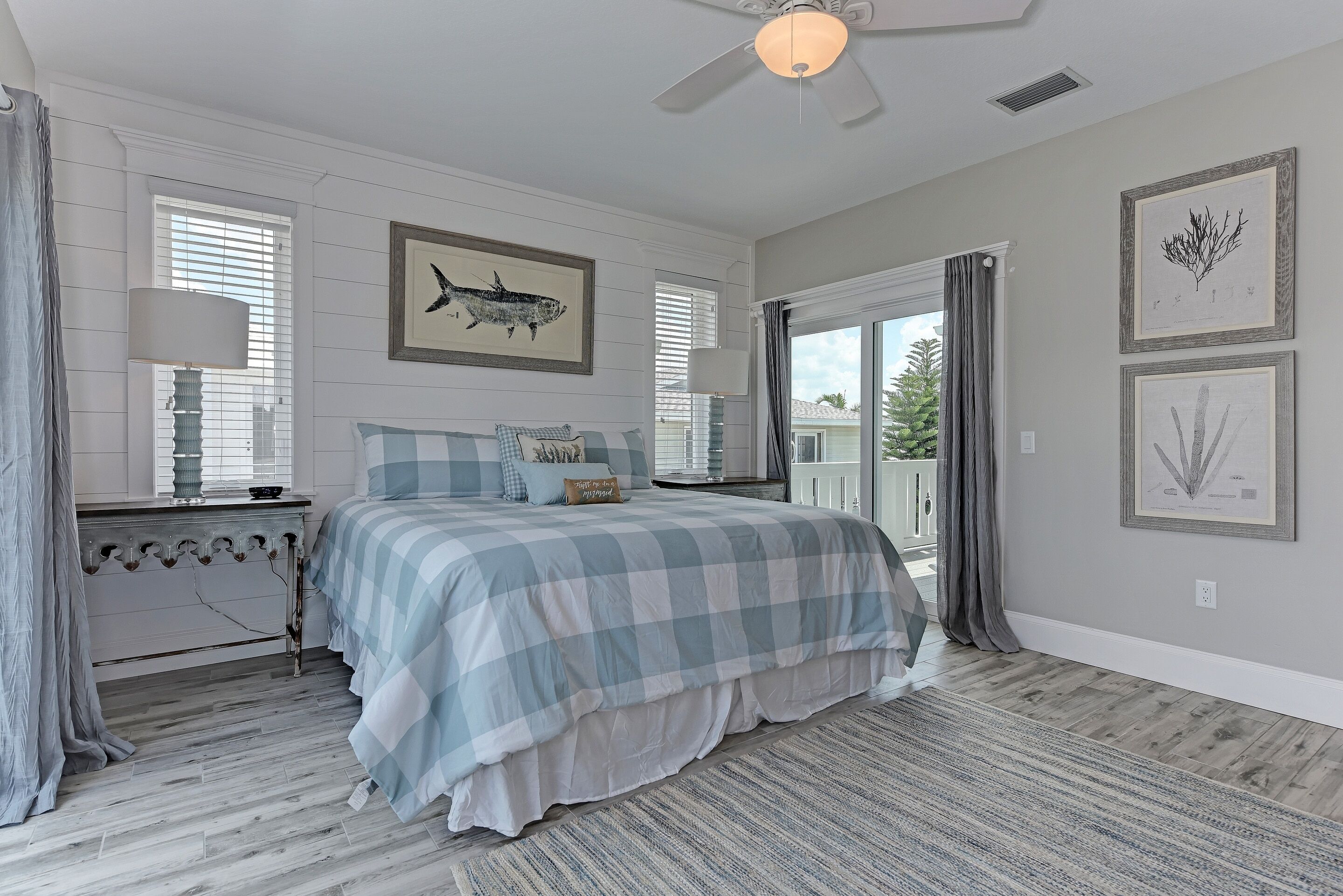 A bedroom with a checkered bedspread, a ceiling fan, and framed artwork on the walls.