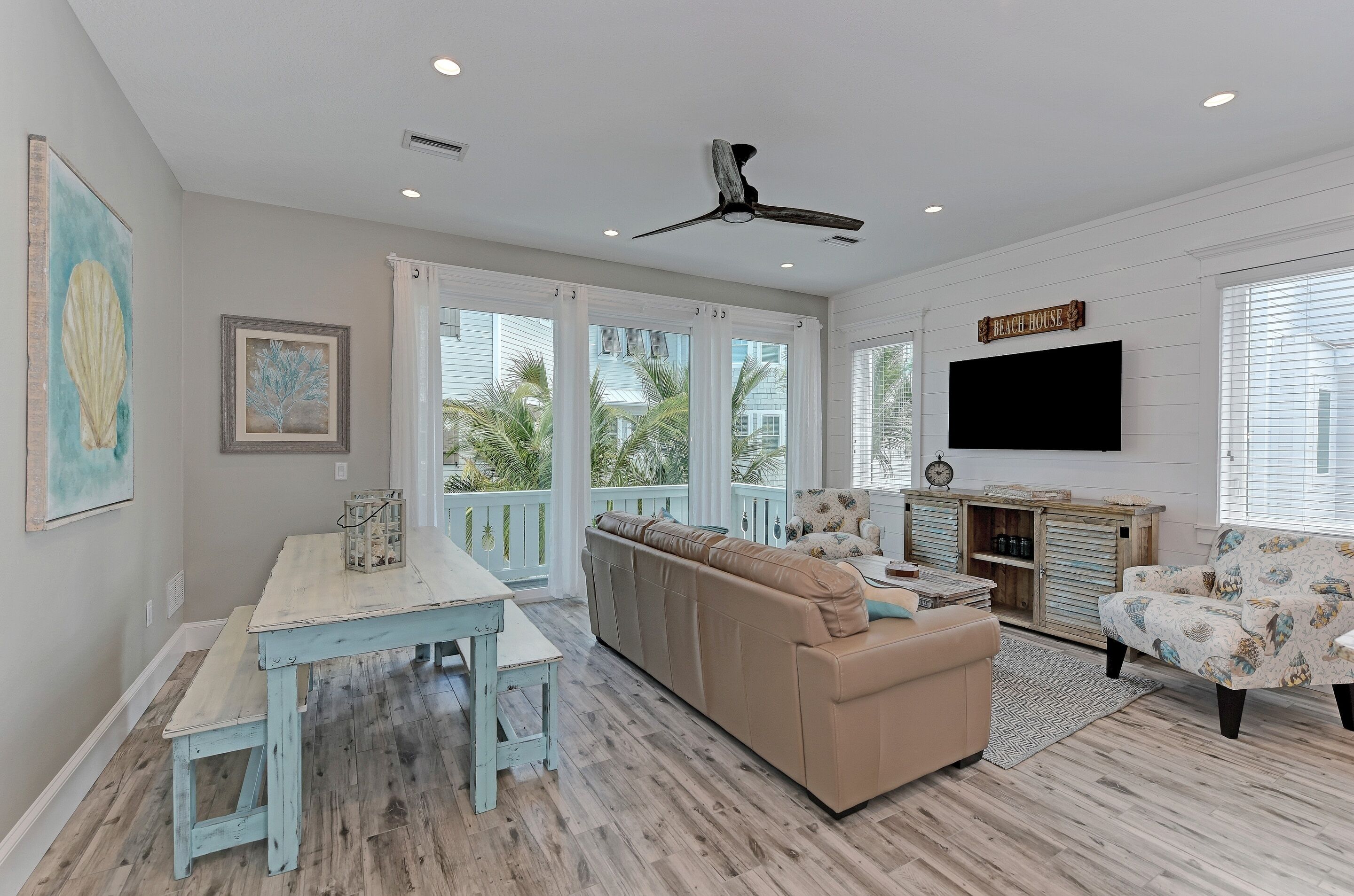A spacious living room with a large beige sofa, a wooden coffee table, a patterned armchair, and a dining area with a blue table and bench.