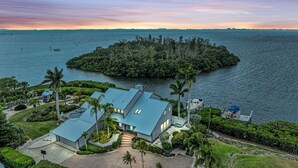 Une maison moderne avec un toit bleu, entourée d’une végétation luxuriante et bordée par un plan d’eau.