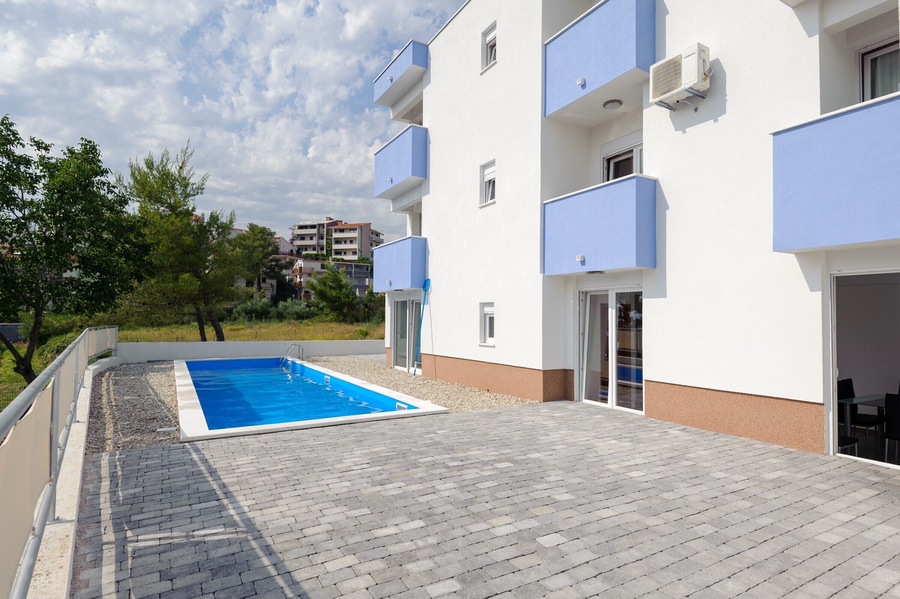 A modern building with a swimming pool, balconies, and a paved patio area.