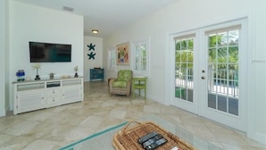 A spacious living area with a television, a console table, a chair, and a door leading outside. - Footprints in the Sand managed by Beach Retreats (Holmes Beach)