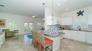 A spacious kitchen with white cabinetry, a central island with chairs, and a ceiling fan. - Footprints in the Sand managed by Beach Retreats (Holmes Beach)