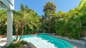 A swimming pool surrounded by lush tropical vegetation, including palm trees and various shrubs. - Footprints in the Sand managed by Beach Retreats (Holmes Beach)