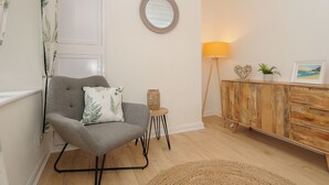 A modern living room with a grey armchair, a small side table, a wooden cabinet, and a floor lamp. - Carvannel Cottages (Camborne)