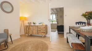 A dining area with a wooden table set for four, a woven rug, and a cabinet with decorative items. - Carvannel Cottages (Camborne)