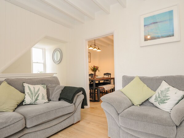 A cozy living room with two grey sofas, each with a green and white pillow, and a dining area with a wooden table and chairs.
