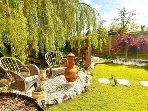 Un jardí amb cadires de vimetla, una olla de terracota gran i una petita bassa.