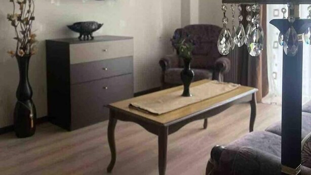 A living room with a television, a dark-colored sofa, a wooden coffee table, and a chandelier. - Nearby Chavchavadze ave Sunny Home With Balcony (Tbilisi)